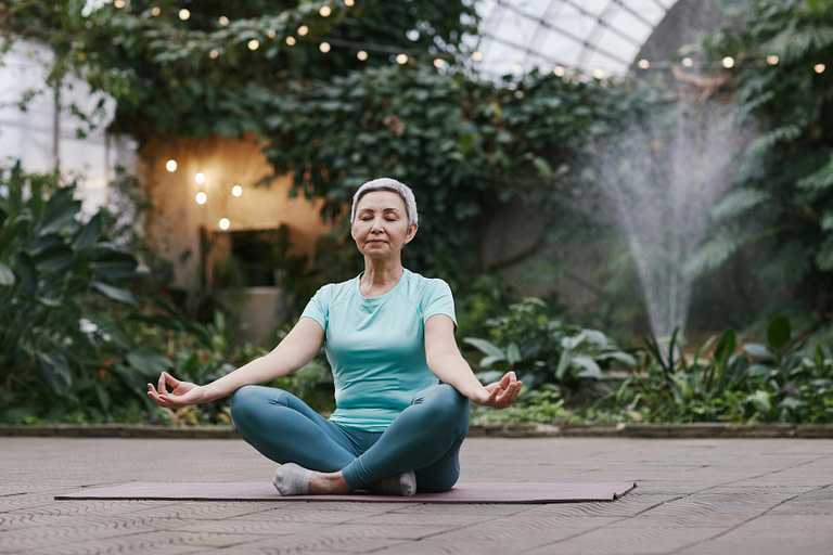 Woman Sitting on floor in a meditation pose inside a botanical greenhouse.